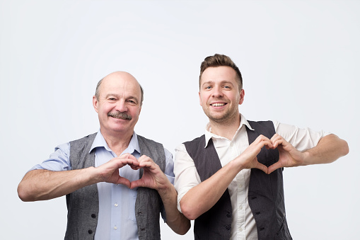 Two happy caucasian men show heart gesture with hands. Charity, volunteer concept