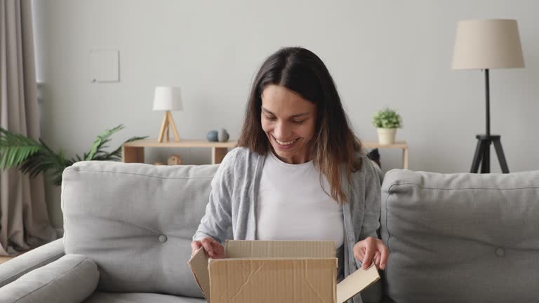 Amazed young woman opening cardboard box with internet store order.