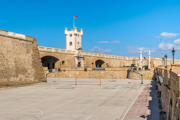 Plaza de la Constitucion with Puertas de Tierra in Cadiz, Spain Plaza de la Constitucion with Puertas de Tierra, a bastion-monument built around remnants of the old defensive wall with the purple flag of its canton at the entrance to the city of Cadiz, Spain constitucion photos stock pictures, royalty-free photos & images