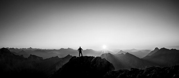 Happy winning success man at sunset or sunrise standing relaxed and is happy for having reached mountain top summit goal during hiking travel trek. Black-and-White. Tirol, Austria. Allgäu, Bavaria.
