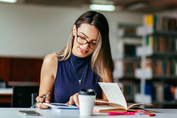 istock Young woman studying at table in library 1210632819