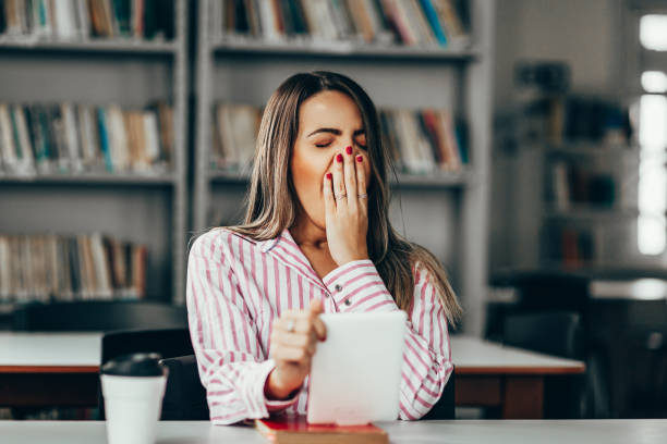 donna assonna che studia a tavola in biblioteca - yawning women drink coffee cup foto e immagini stock