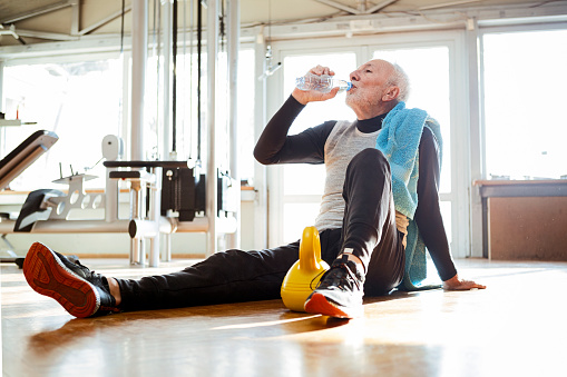 Senior man sitting on floor in a gym hydrating after training