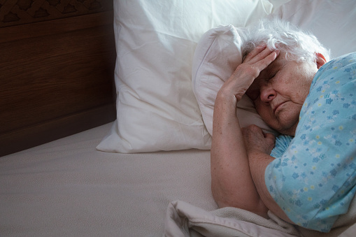 Sick Elderly Woman in Bed trying to sleep, holding her head with her hand.