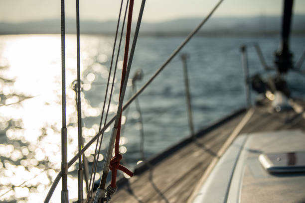 Looking out on the shiny sea full of bokeh, from the teak wooden deck of a sailboat. The railings are chrome.