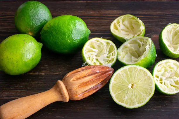 Lime halves and a citrus reamer on a dark wood background