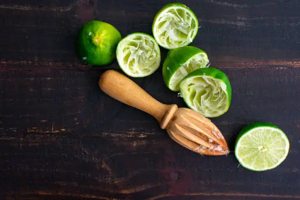 Lime halves and a citrus reamer on a dark wood background