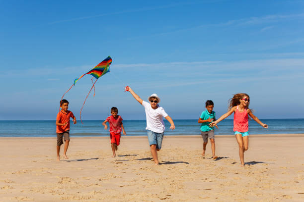 group of many kids run with kite on a sand beach - stripped shirt imagens e fotografias de stock