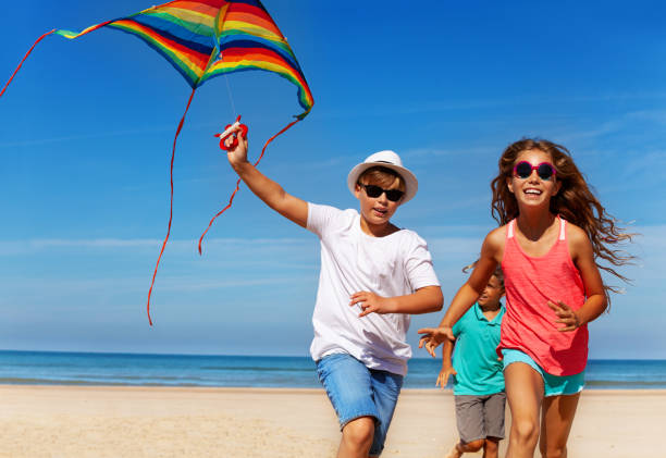 istock Three kids run on the beach with kite 1210659161