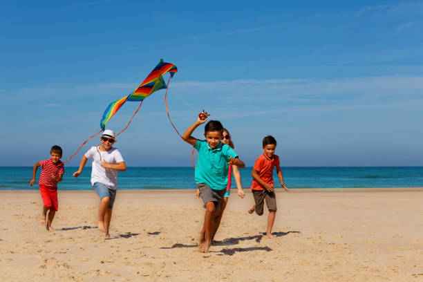 grupa dzieci z kolorowym latawcem na plaży - stripped shirt zdjęcia i obrazy z banku zdjęć