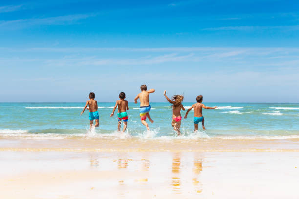 istock Many kids friends run into sea waves on sand beach 1210659190