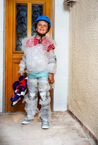 Kid hold rollerblades ball wear super safe bubble wrap and helmet have overprotective mother standing near home door