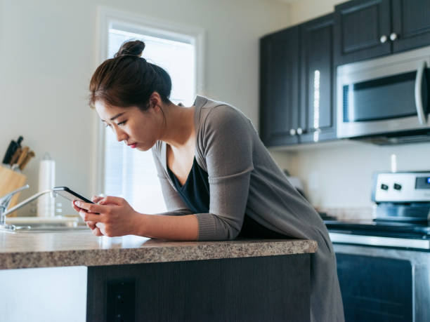 istock asian woman texting in kitchen 1210674830
