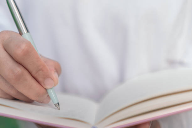 istock Woman hand writing down in small white memo notebook for take a note not to forget or to do list plan for future. 1210681495