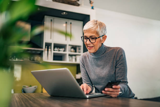 Modern mature woman using laptop and smart phone at home, portrait. Modern mature woman using laptop and smart phone at home, portrait. short hair photos stock pictures, royalty-free photos & images