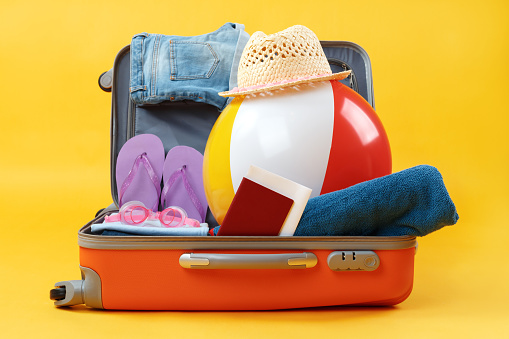 Open full suitcase with items for relaxation on a yellow background.