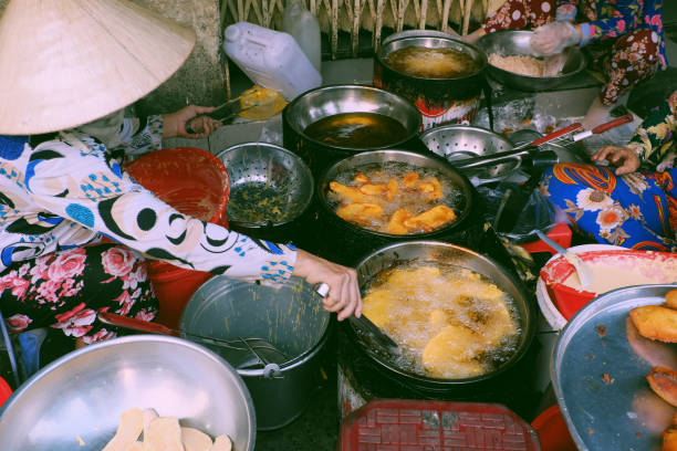 Vietnamese outdoor food street at Ho Chi Minh city in evening, tray of crispy snacks cake from powder deep fried in cooking oil so delicious for ready to eat, boiling oil pan on charcoal stove