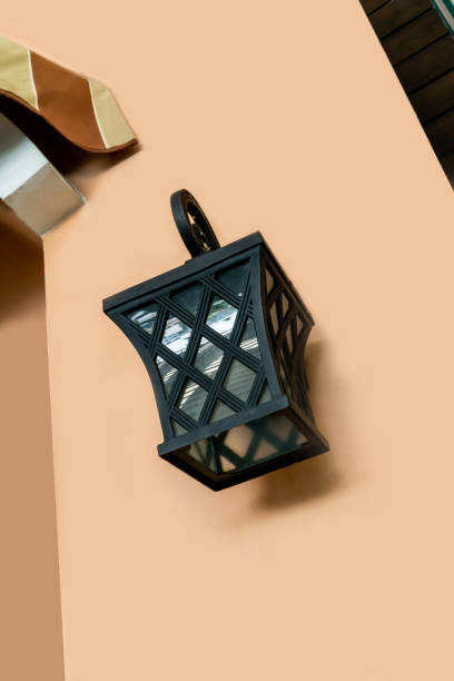 Black metal classic lamp with warm white light bulb hanging against orange wall.