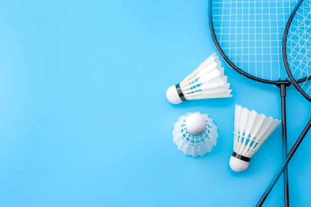 Photo of Competitive sports and high performance in tournament match conceptual idea with badminton rackets and shuttlecock (birdie) isolated on blue court background with copy space