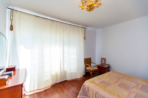 istock A large bedroom with a mahogany bed, wicker chairs, and an elegant dressing table with a semi-circular mirror. The bed has a beige blanket in squares. mahogany parquet 1210696645