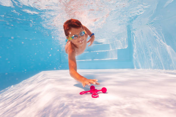 istock Cute boy dive and swim for toy on pool bottom 1210697802