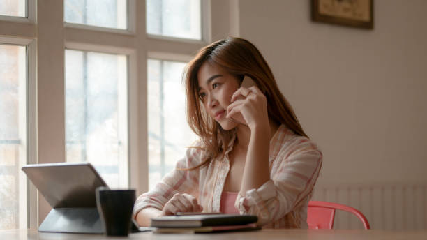 istock Cropped shot of young college girl calling while working on her assignment with tablet and stationery 1210707924