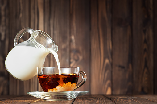 flying jug pouring milk into cup of tea on wooden table