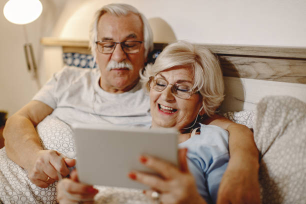 istock Happy senior woman and her husband using touchpad while relaxing in bed. 1210708951