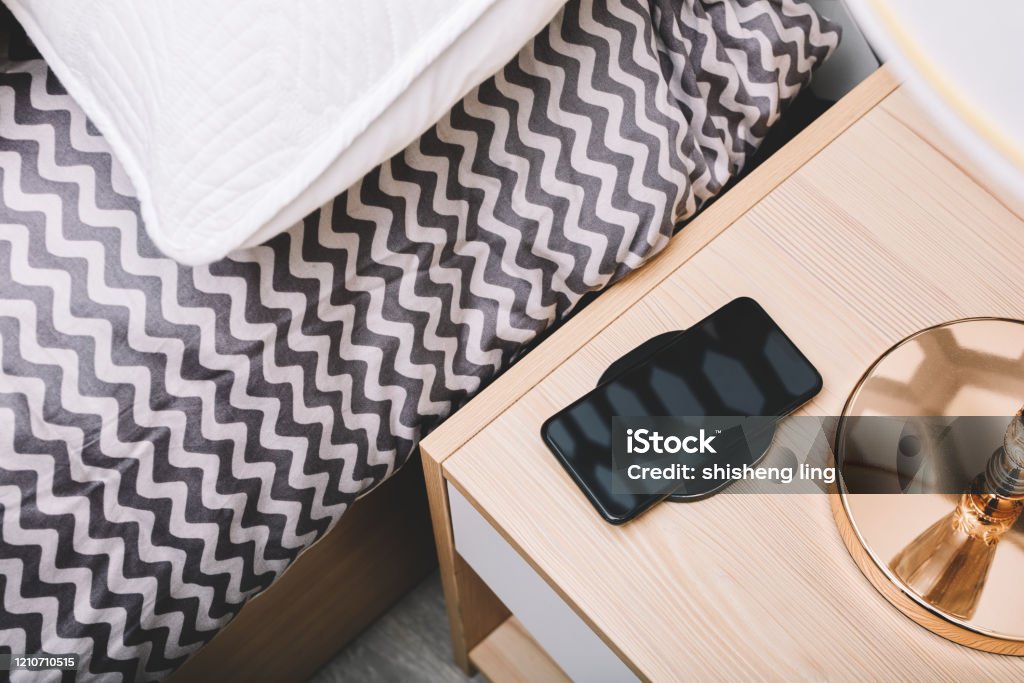 The mobile phone in the bedside wireless charging is in the bedroom The mobile phone in the bedside wireless charging is in the bedroom，Science and technology life concept Night Table Stock Photo