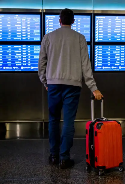 Photo of Passenger looking at timetable board at the airport. Man in international airport looking at the flight information board