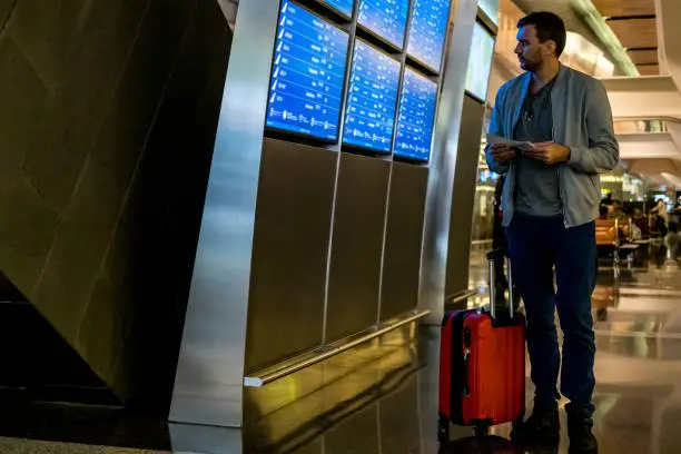 Photo of Passenger looking at timetable board at the airport. Man in international airport looking at the flight information board