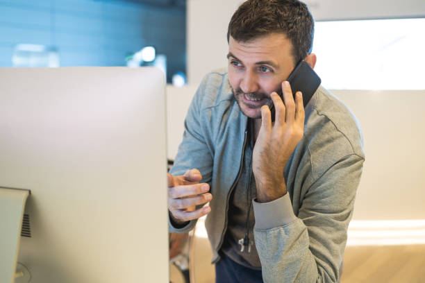 istock Casual businessman working at office desk, using mobile phone and laptop computer, typing, making phone call, smiling. 1210715733