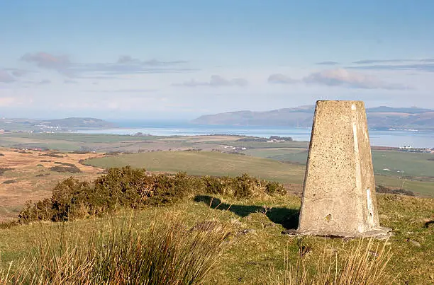 Triangulation point (trig point) on top of a hill with a view over sea loch Loch Ryan behind. Trig points were used by Ordnance Survey in the UK as aids to drawing up geographical maps. This particular one is on Cairnpat on the Rhins of Galloway in South West Scotland.