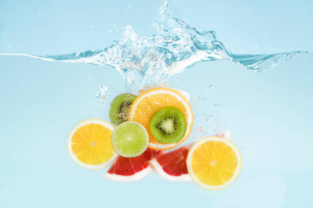 istock Sliced tropical fruits falling into transparent water with splashes on blue background 1210727497