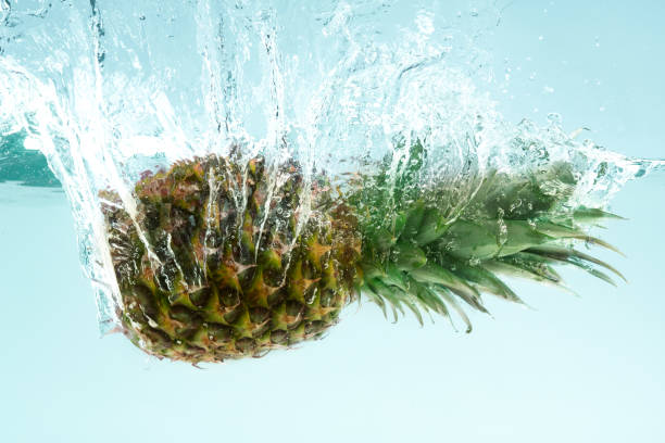 istock Whole organic pineapple splashing into clear water on blue background 1210727669