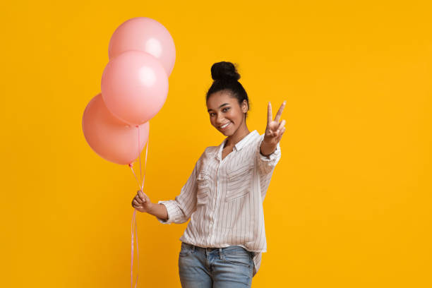 портрет смеющихся афро девушка с розовыми воздушными шарами, показывающие знак мира - balloon pink black anniversary стоковые фото и изображения