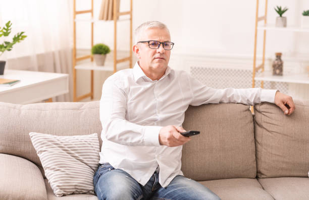 istock Elderly man watching tv sitting on sofa 1210731124