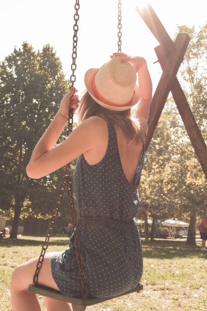Cute young woman enjoying on a swing outdoors in summertime sunlight.