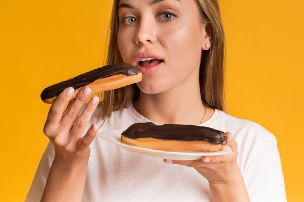 istock Young Woman Eating Eclairs With Chocolate Cream And Looking At Camera 1210733407