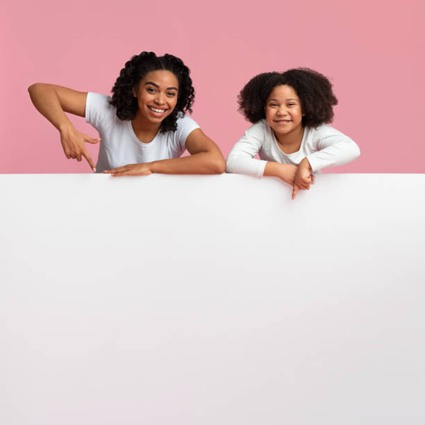 istock Happy Afro Mom And Daughter Pointing At White Advertisement Board 1210736543