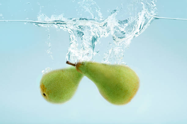 Two green pears falling into transparent water on blue background Two fresh green pears falling into transparent water on blue background perfect pear stock pictures, royalty-free photos & images