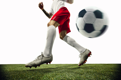 Football or soccer player on white background with grass. Young male sportive model training. Attacking, catching. Concept of sport, competition, winning, action, motion, overcoming. Wide angle.