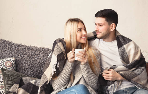 istock Smiling young couple with hot drinks cuddling under warm blanket at home, empty space 1210737211