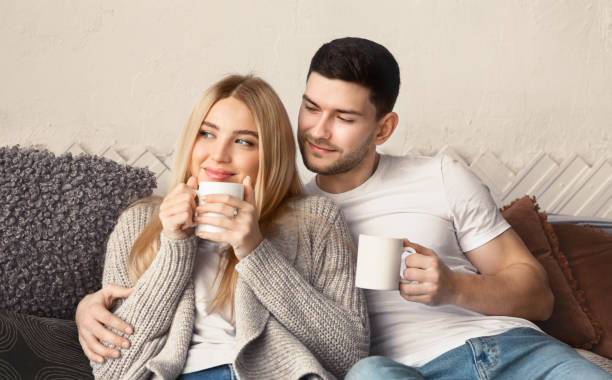 istock Affectionate couple with hot drinks cuddling on sofa in living room 1210737226