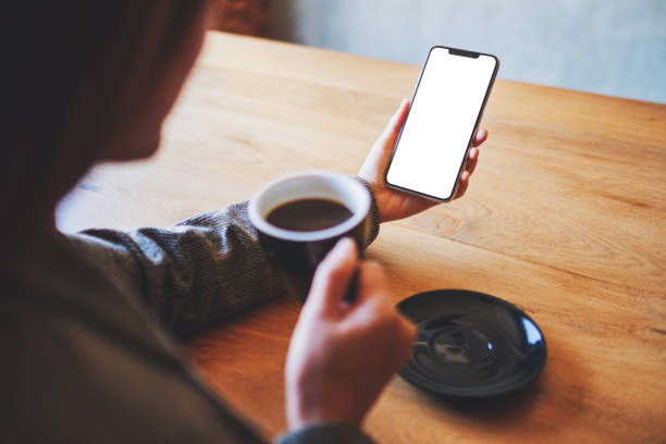 istock a woman holding mobile phone with blank white screen while drinking coffee on wooden table 1210738117