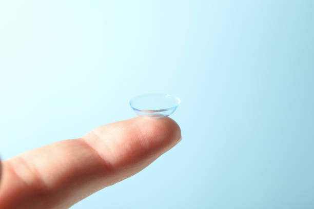 istock Finger with contact lens on blue background, close up 1210738529
