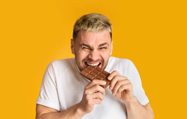 istock Man sweet tooth happily bites chocolate isolated on yellow background 1210741330