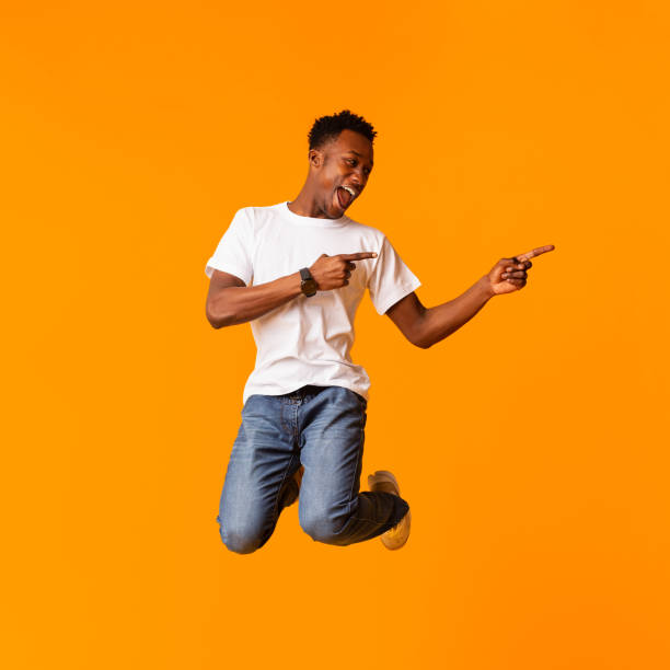 istock Stylish african guy jumping and gesturing on orange 1210741985
