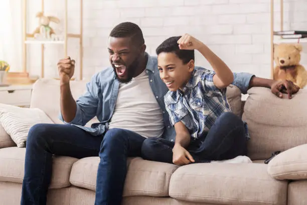 Family Cheering. Afro Dad And Son Emotionally Supporting Their Favorite Team, Watching Sports On Tv At Home Together, Free Space