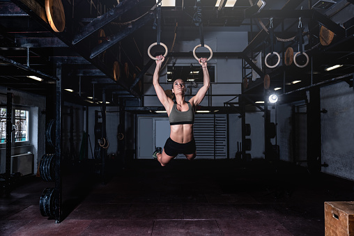 Young attractive muscular strong fit girl swinging on gymnastic ring heavy hardcore cross workout swing workout training in the gym real people exercising